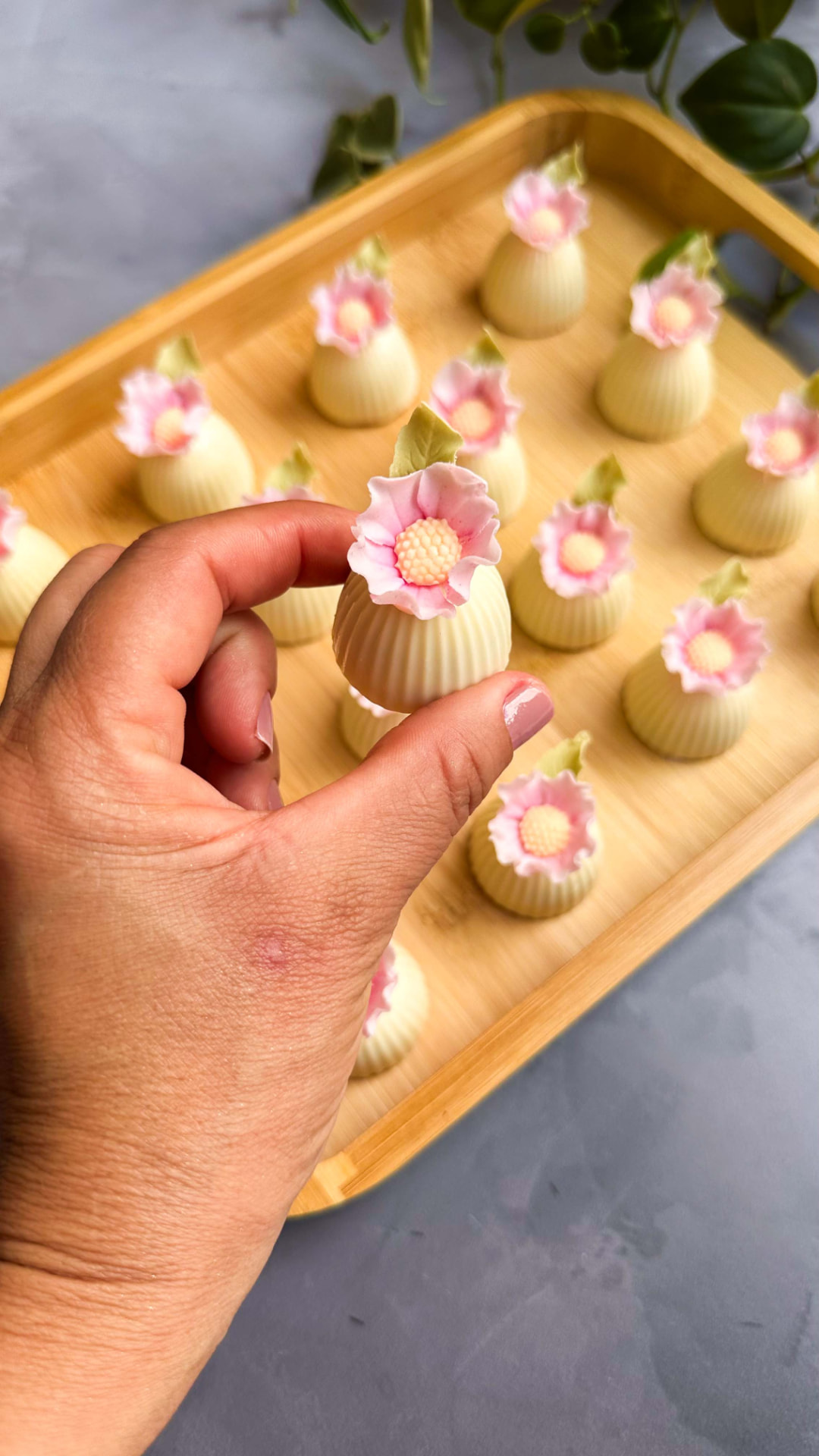 Mão segurando brigadeiro com mini flor rosa sobre bandeja