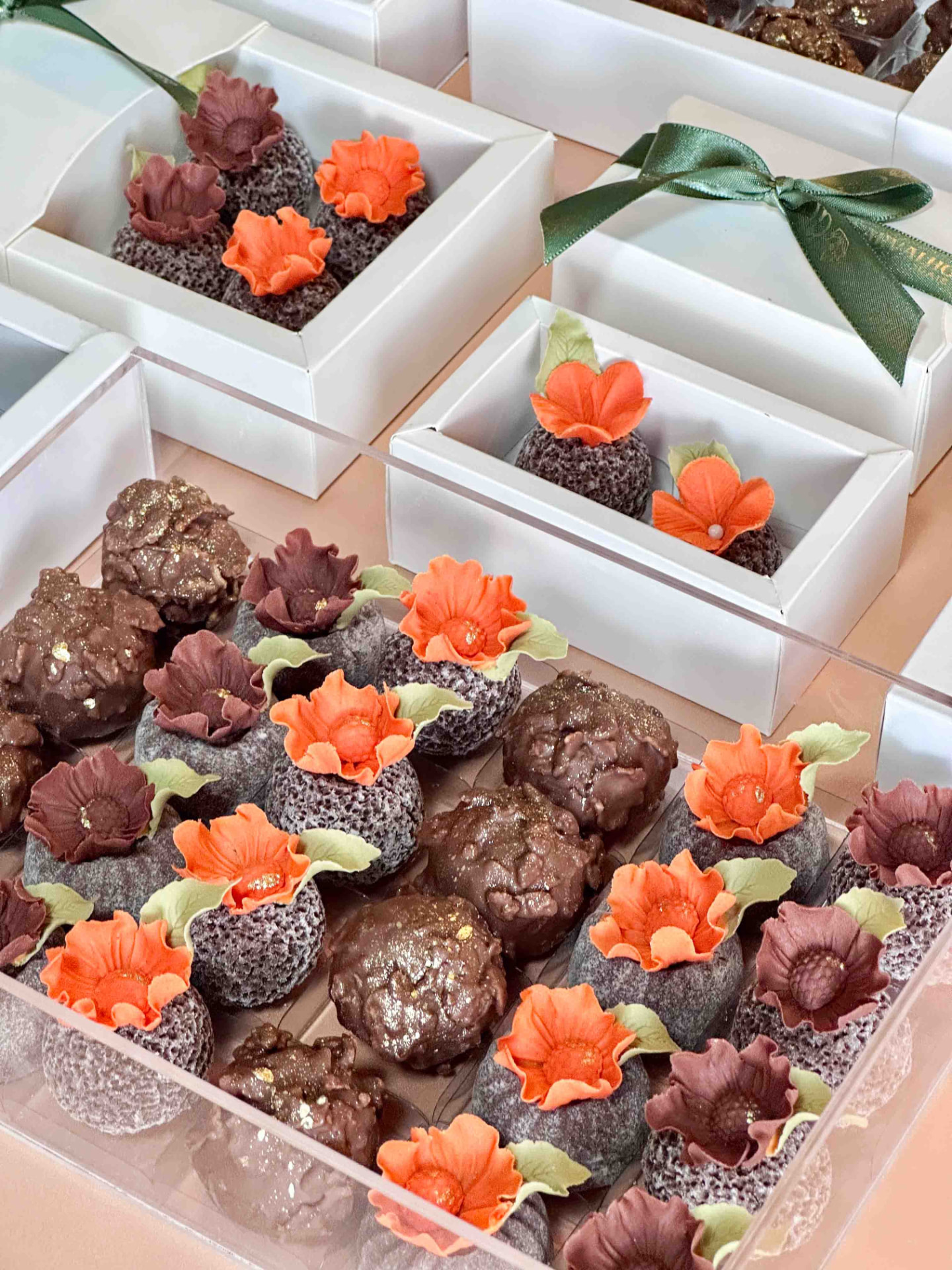 Brigadeiros com mini flores laranja e vinho em caixas brancas